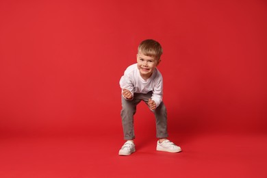 Photo of Happy little boy dancing on red background