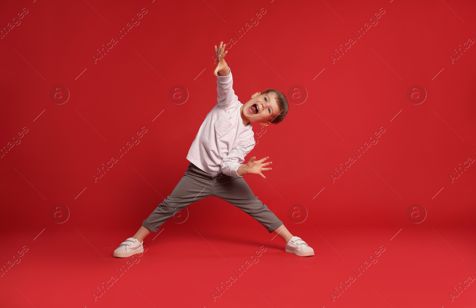 Happy little boy dancing on red background, space for text Photo of Happy little boy dancing on red background, space for text