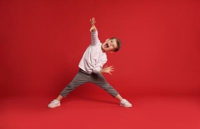 Photo of Happy little boy dancing on red background, space for text