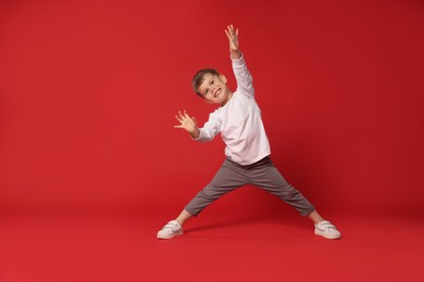 Photo of Happy little boy dancing on red background, space for text