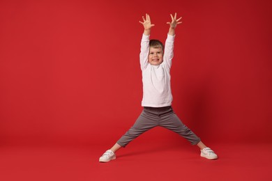 Photo of Happy little boy dancing on red background, space for text