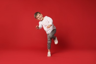 Photo of Happy little boy dancing on red background