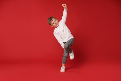 Photo of Happy little boy dancing on red background