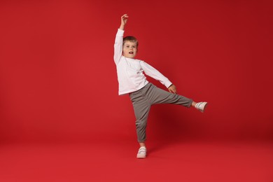 Photo of Happy little boy dancing on red background, space for text