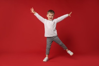 Photo of Happy little boy dancing on red background, space for text