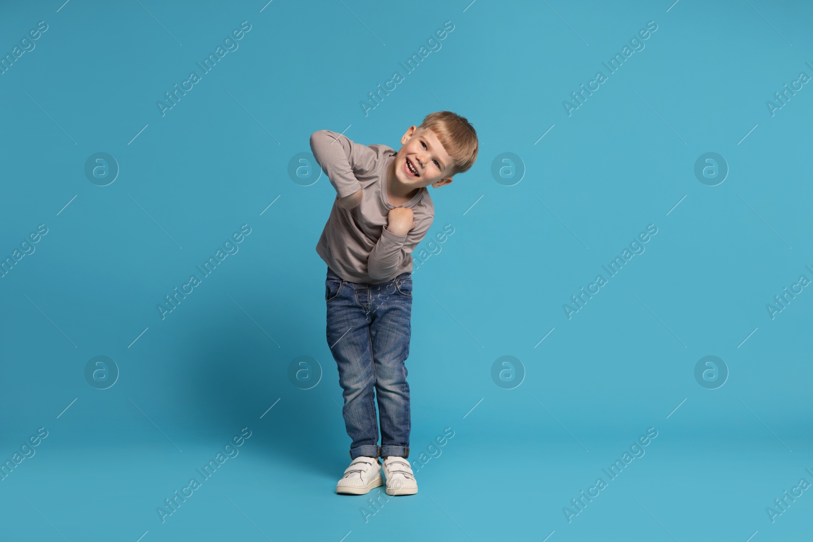 Happy little boy dancing on light blue background Photo of Happy little boy dancing on light blue background