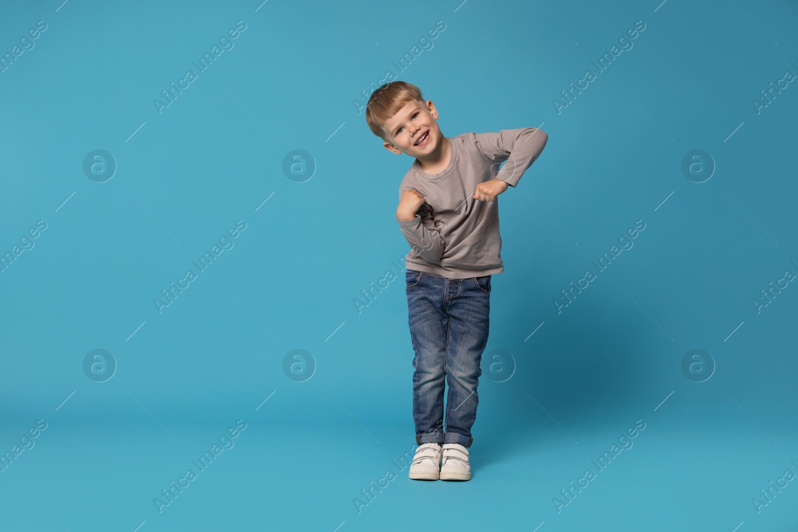 Happy little boy dancing on light blue background, space for text Photo of Happy little boy dancing on light blue background, space for text