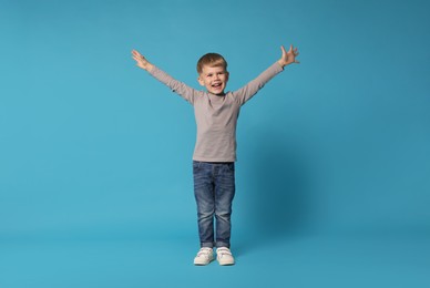 Photo of Happy little boy dancing on light blue background