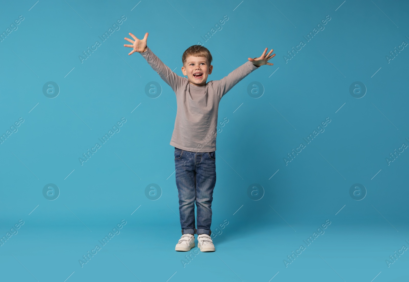 Happy little boy dancing on light blue background Photo of Happy little boy dancing on light blue background