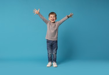 Photo of Happy little boy dancing on light blue background
