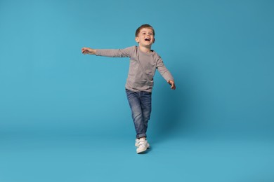 Photo of Happy little boy dancing on light blue background
