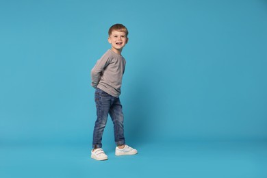 Photo of Happy little boy dancing on light blue background, space for text