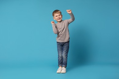 Photo of Happy little boy dancing on light blue background