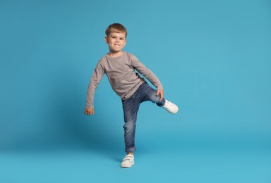 Photo of Happy little boy dancing on light blue background