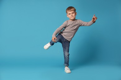 Photo of Happy little boy dancing on light blue background, space for text