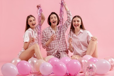 Photo of Pajama party. Happy friends with glasses, balloons and tinsel on pink background