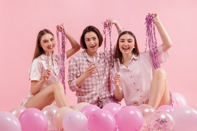 Photo of Pajama party. Happy friends with glasses, balloons and tinsel on pink background