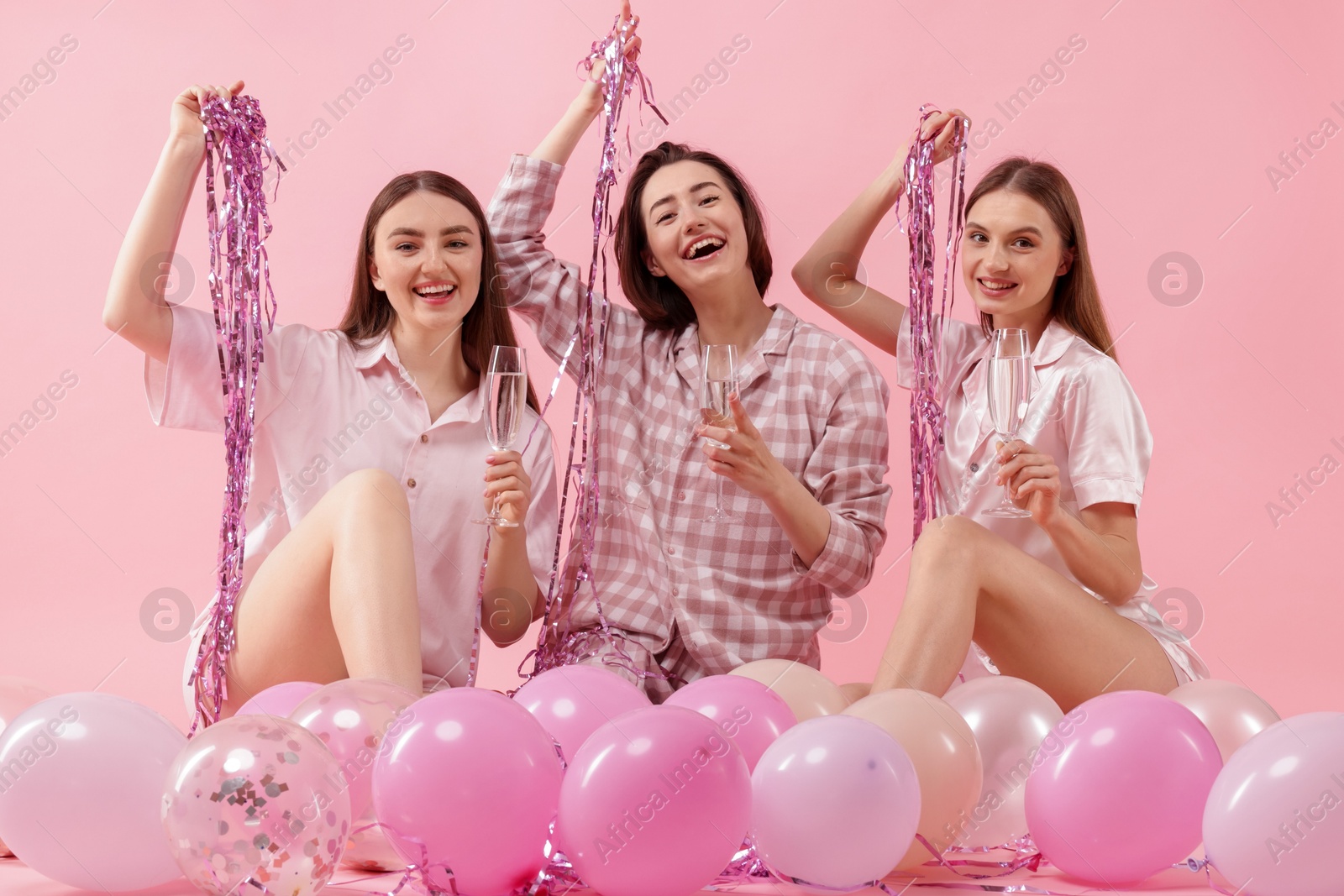 Pajama party. Happy friends with glasses, balloons and tinsel on pink background Photo of Pajama party. Happy friends with glasses, balloons and tinsel on pink background