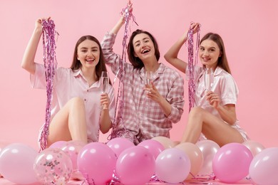 Photo of Pajama party. Happy friends with glasses, balloons and tinsel on pink background