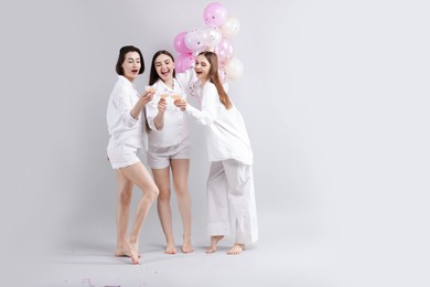 Photo of Pajama party. Happy friends with balloons clinking glasses on grey background