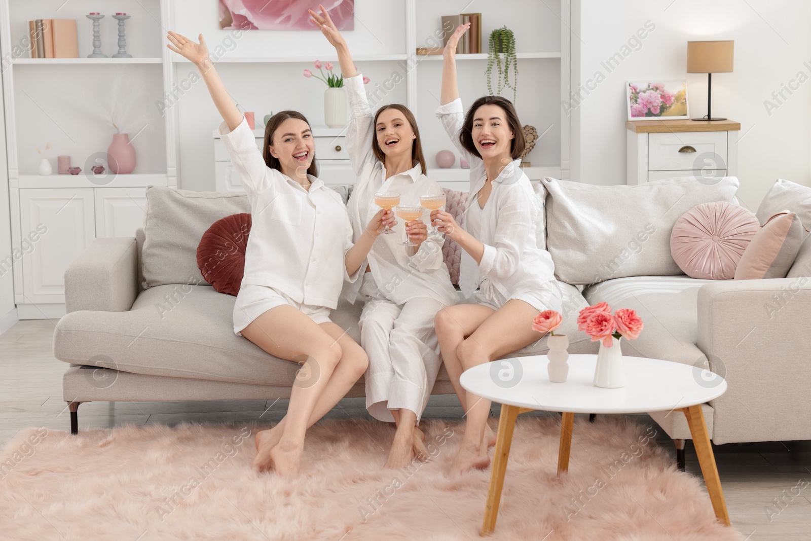 Pajama party. Happy friends clinking glasses on sofa at home Photo of Pajama party. Happy friends clinking glasses on sofa at home