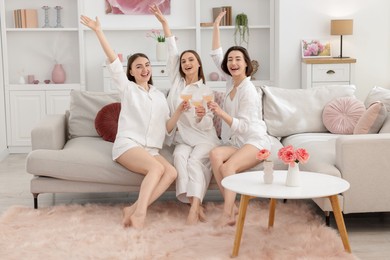 Photo of Pajama party. Happy friends clinking glasses on sofa at home