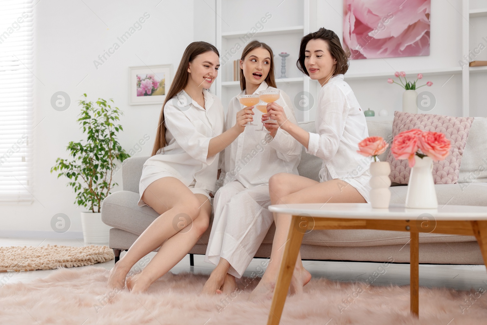 Pajama party. Happy friends clinking glasses on sofa at home Photo of Pajama party. Happy friends clinking glasses on sofa at home