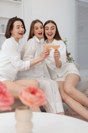 Photo of Pajama party. Happy friends clinking glasses on sofa at home