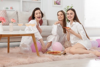 Photo of Happy friends in pajamas eating pizza on floor at home