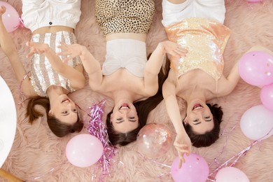 Photo of Happy friends with balloons and tinsel on faux fur, top view