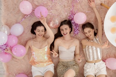 Photo of Happy friends with balloons and tinsel on faux fur, top view