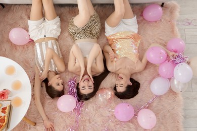 Photo of Happy friends with balloons and tinsel on floor at home, top view