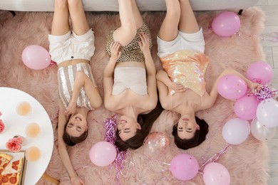 Photo of Happy friends with balloons and tinsel on floor at home, top view