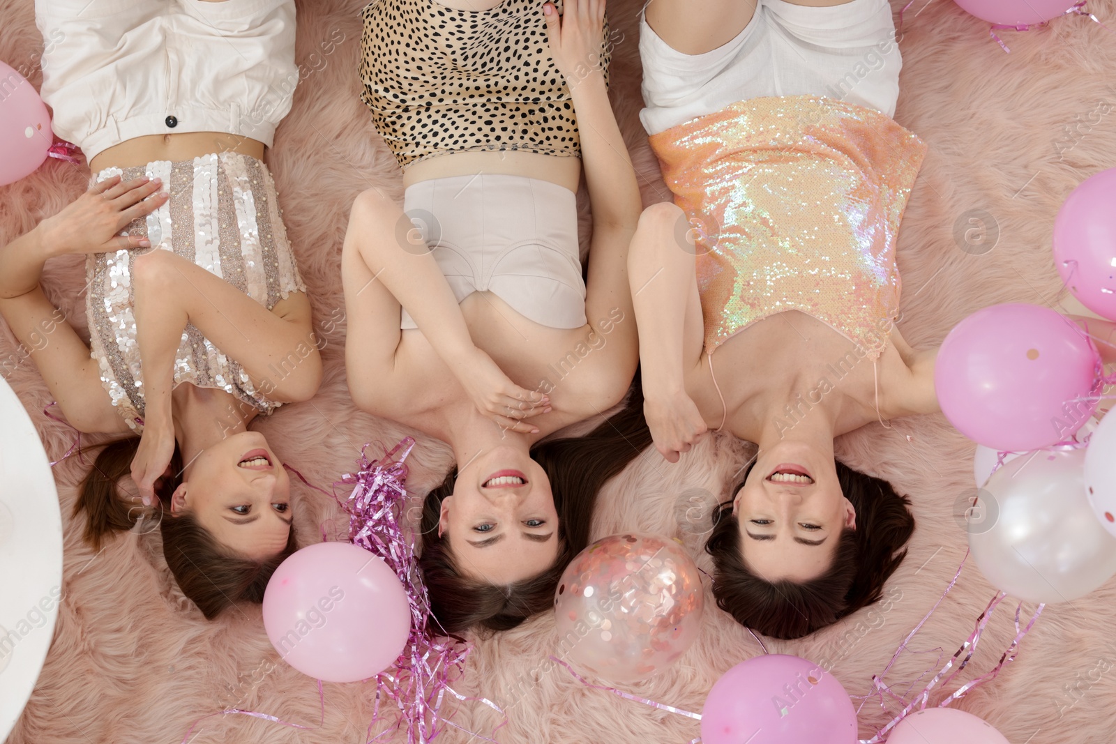 Happy friends with balloons and tinsel on faux fur, top view Photo of Happy friends with balloons and tinsel on faux fur, top view