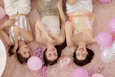 Photo of Happy friends with balloons and tinsel on faux fur, top view