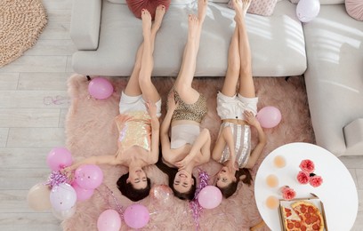 Photo of Happy friends with balloons and tinsel on floor at home, top view