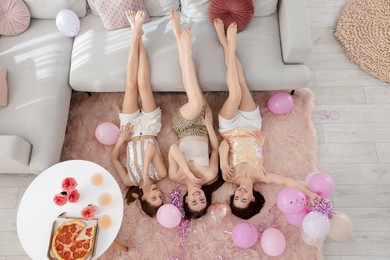 Photo of Happy friends with balloons and tinsel on floor at home, top view
