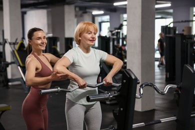 Photo of Senior woman exercising with EZ curl bar supervised by professional trainer in gym