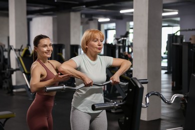 Photo of Senior woman exercising with EZ curl bar supervised by professional trainer in gym