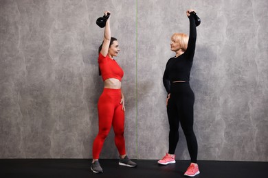 Photo of Senior woman and professional trainer training with kettlebells in gym