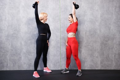 Photo of Senior woman and professional trainer training with kettlebells in gym