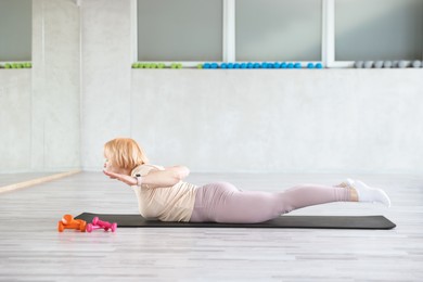 Photo of Senior woman exercising on fitness mat in gym
