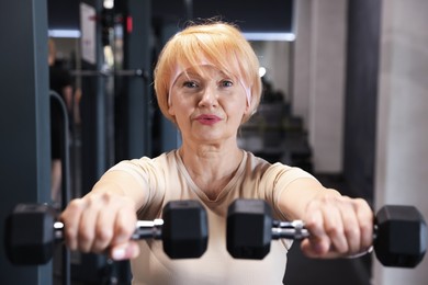 Photo of Senior woman training with dumbbells in gym