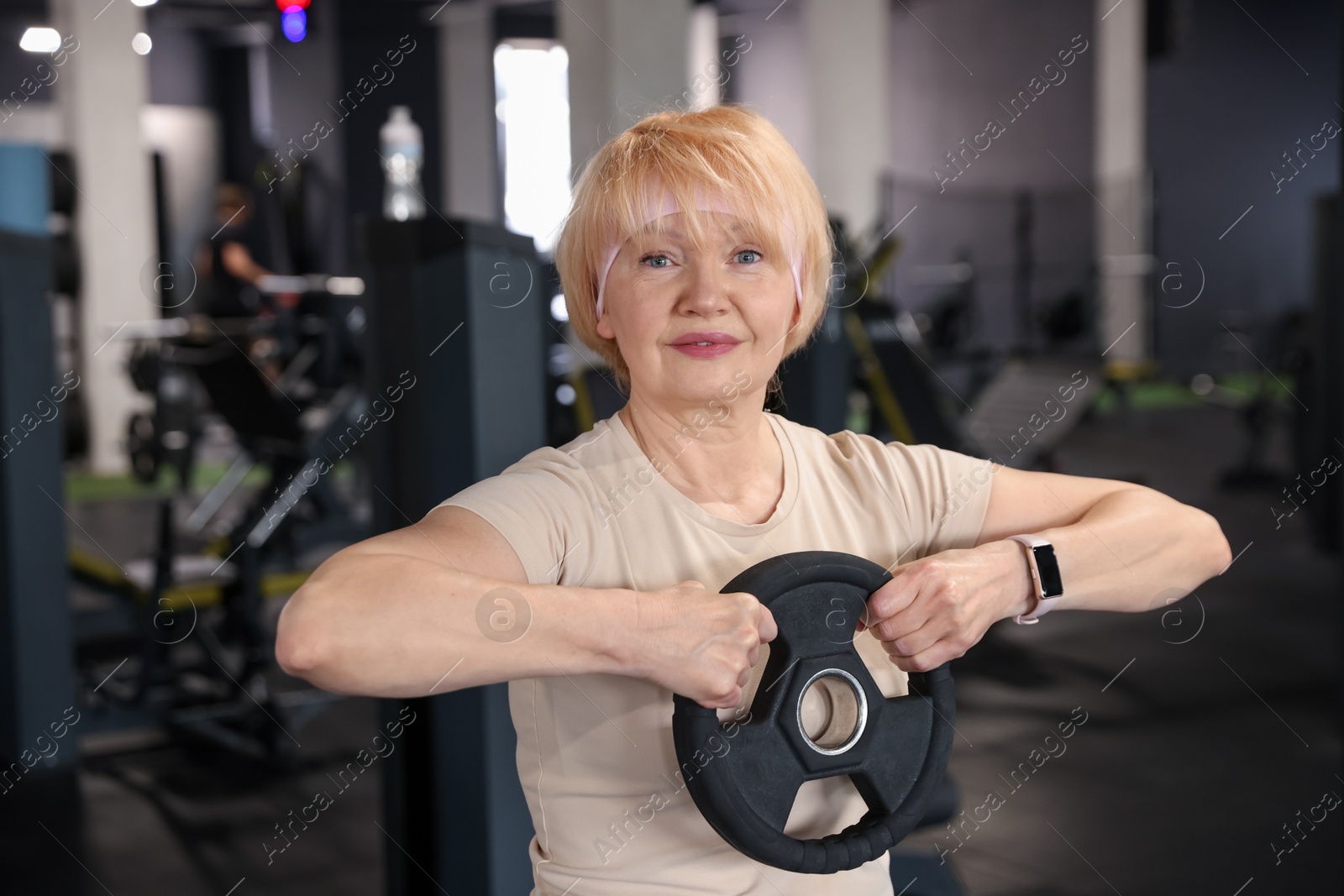 Senior woman training with weight plate in gym Photo of Senior woman training with weight plate in gym