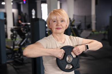 Photo of Senior woman training with weight plate in gym
