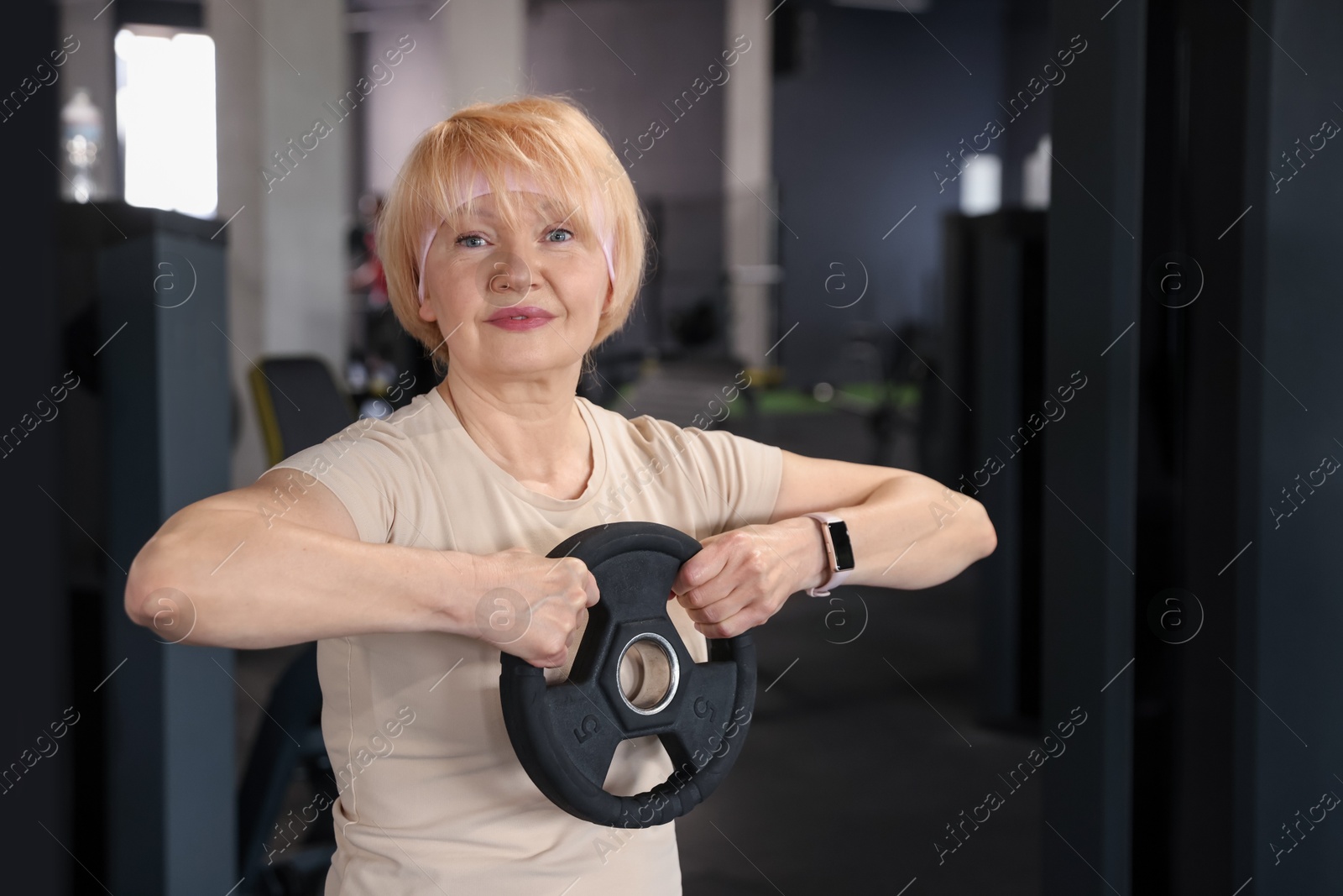 Senior woman training with weight plate in gym Photo of Senior woman training with weight plate in gym