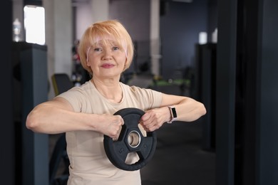 Photo of Senior woman training with weight plate in gym