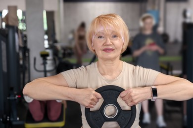 Photo of Senior woman training with weight plate in gym