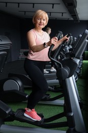 Photo of Senior woman training on elliptical machine in gym