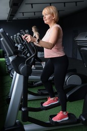 Photo of Senior woman training on elliptical machine in gym